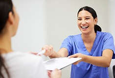 Dental assistant smiling while handing patient form