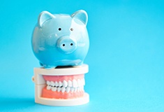 Piggy bank atop model teeth representing the cost of dental implants in Forest