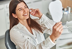Woman smiling at reflection in handheld mirror