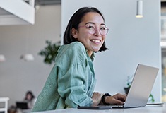 Woman with glasses smiling while working on laptop