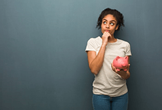 a woman thinking and holding a piggy bank