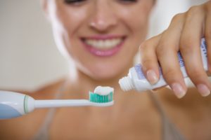 woman putting toothpaste on electric toothbrush 